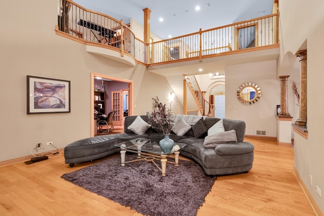 living room with decorative columns, a high ceiling, and light wood-type flooring