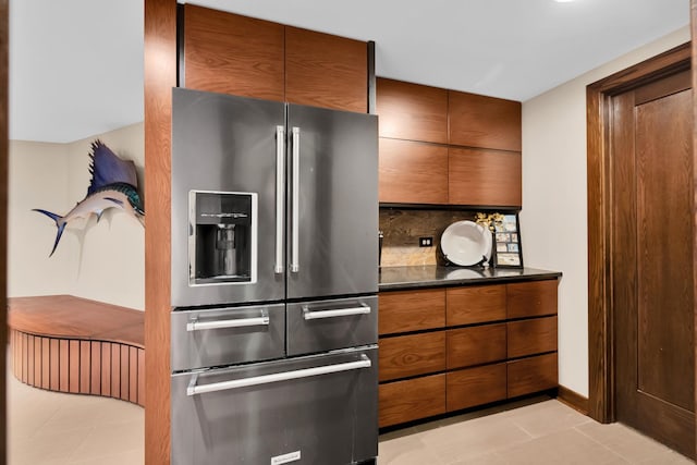 kitchen featuring high quality fridge, dark stone countertops, backsplash, and light tile patterned floors