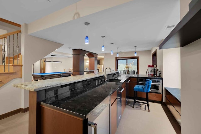 bar with sink, decorative light fixtures, stainless steel oven, and stone countertops