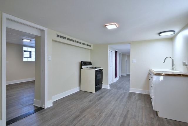 kitchen featuring range with gas stovetop, dark wood finished floors, a sink, and baseboards