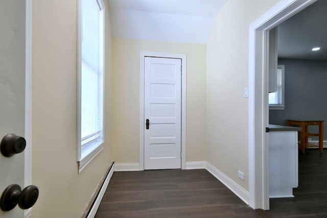 corridor featuring a baseboard heating unit, baseboards, and dark wood-type flooring