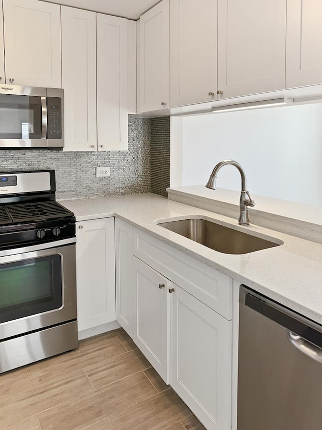 kitchen featuring sink, stainless steel appliances, light stone counters, tasteful backsplash, and white cabinets