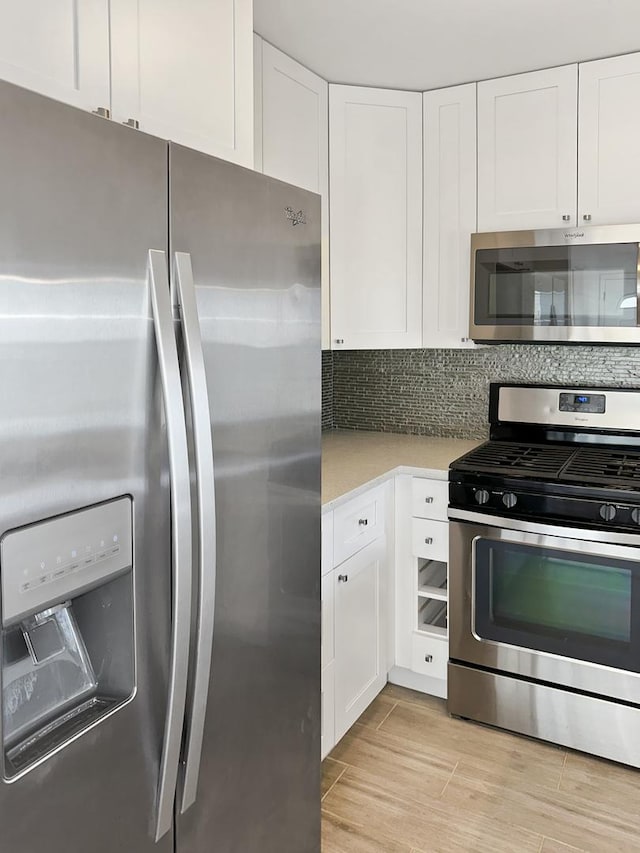 kitchen with stainless steel appliances, white cabinets, light wood-type flooring, and decorative backsplash