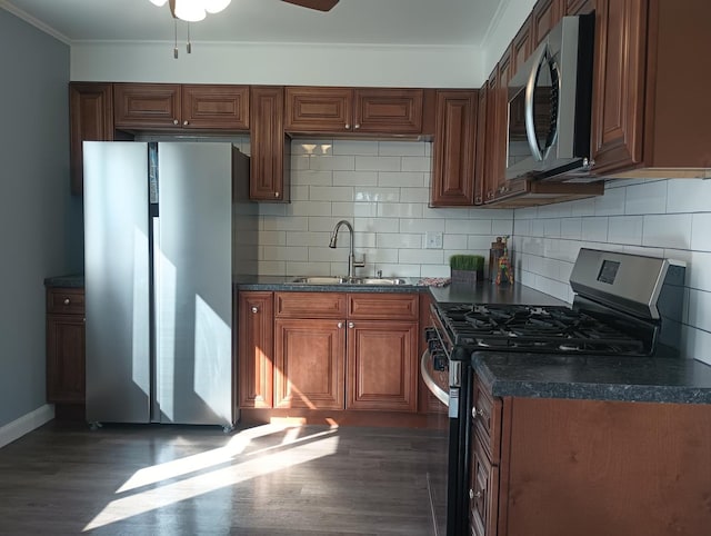 kitchen with dark wood-type flooring, a sink, dark countertops, stainless steel appliances, and crown molding