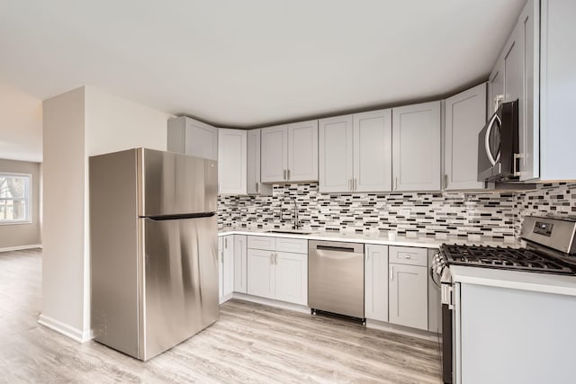 kitchen with appliances with stainless steel finishes, sink, light hardwood / wood-style flooring, and backsplash