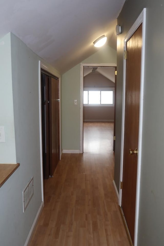 hall with visible vents, baseboards, wood finished floors, and lofted ceiling