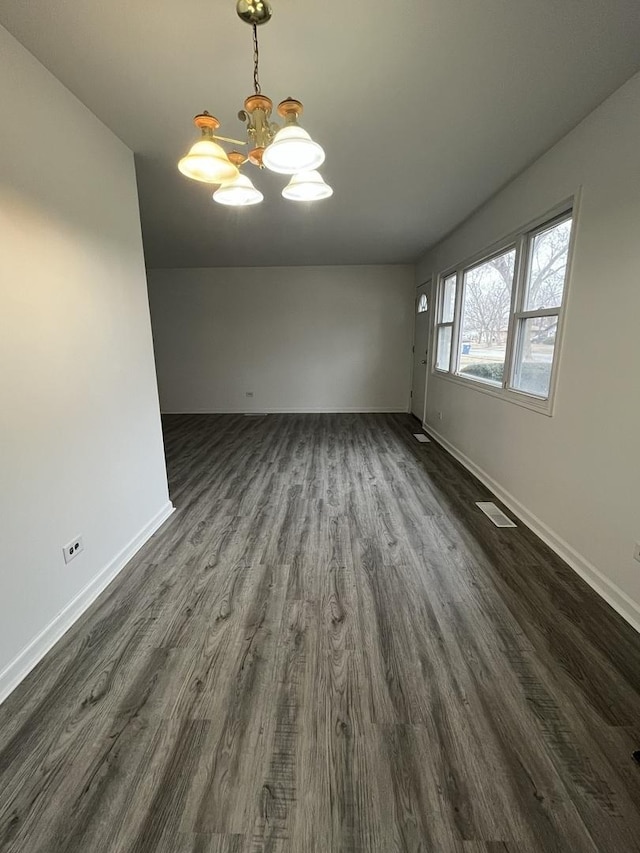 empty room with dark wood-type flooring and a chandelier