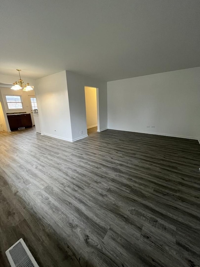 unfurnished living room featuring dark wood-type flooring and a notable chandelier