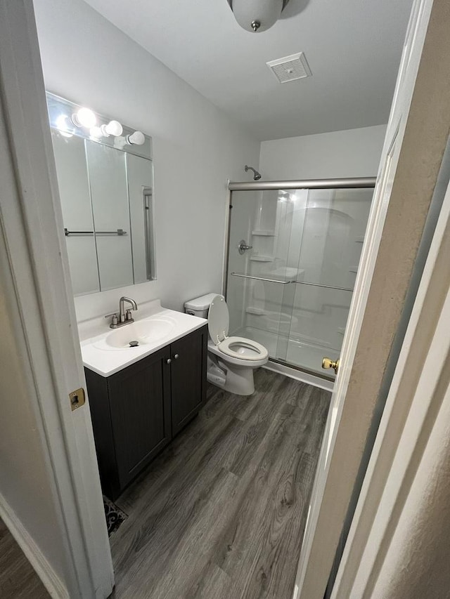 bathroom with vanity, hardwood / wood-style floors, a shower with shower door, and toilet