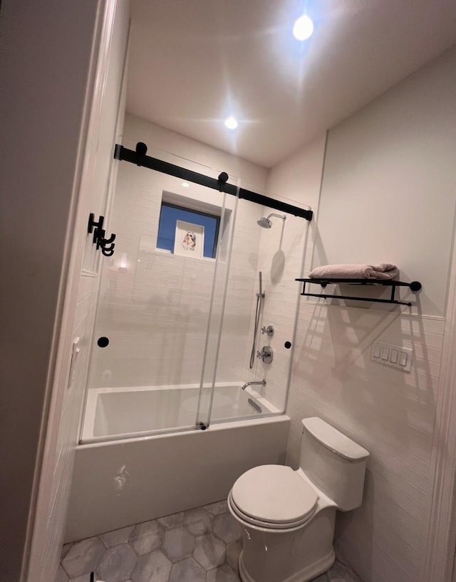 bathroom with tile walls, shower / bath combination with glass door, and toilet