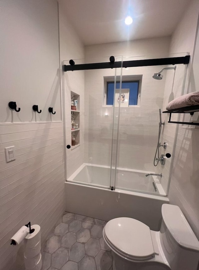 bathroom featuring combined bath / shower with glass door, tile walls, tile patterned floors, and toilet