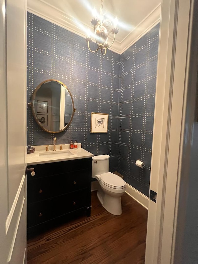 bathroom featuring an inviting chandelier, vanity, wood-type flooring, ornamental molding, and toilet