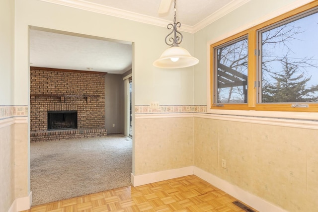 unfurnished dining area featuring ornamental molding, visible vents, wainscoting, and a brick fireplace