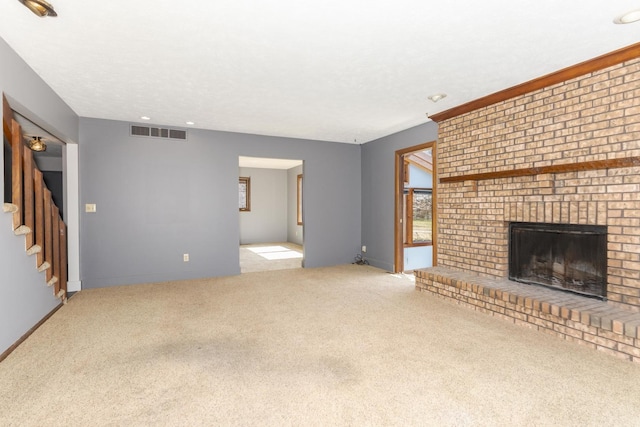 unfurnished living room featuring stairway, carpet, baseboards, visible vents, and a brick fireplace