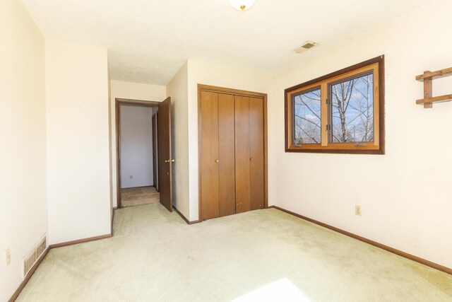 unfurnished bedroom with a closet, baseboards, visible vents, and light colored carpet