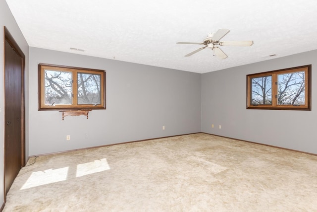 spare room featuring a textured ceiling, a wealth of natural light, a ceiling fan, and light carpet