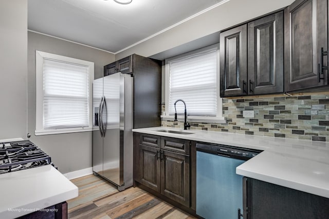 kitchen with dark brown cabinetry, sink, light wood-type flooring, appliances with stainless steel finishes, and decorative backsplash