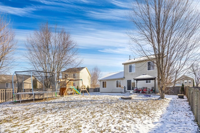 snow covered rear of property featuring a trampoline, a gazebo, and a playground