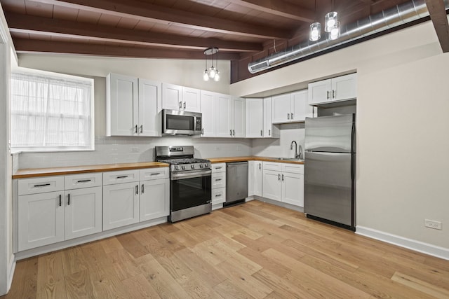 kitchen featuring butcher block countertops, stainless steel appliances, white cabinetry, pendant lighting, and backsplash