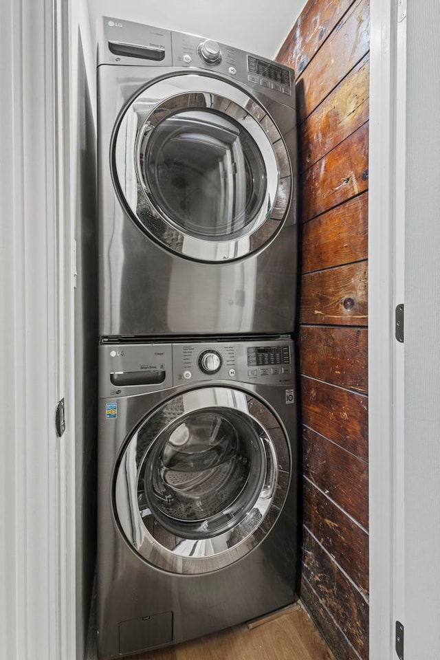 laundry area with stacked washer and dryer, laundry area, wood walls, and wood finished floors