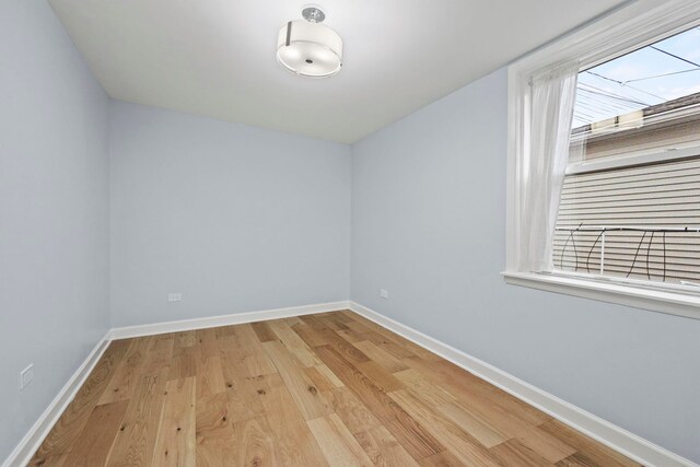 empty room with vaulted ceiling with skylight and light hardwood / wood-style flooring