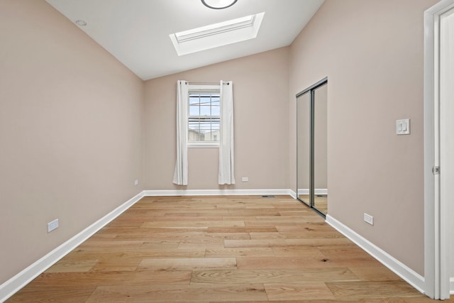 unfurnished bedroom with vaulted ceiling with skylight, light wood finished floors, a closet, and baseboards