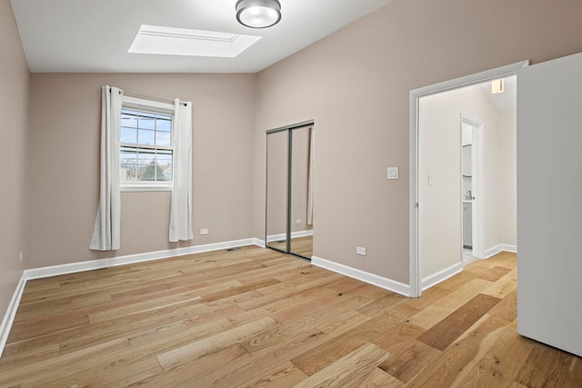 unfurnished bedroom with light wood finished floors, lofted ceiling with skylight, a closet, and baseboards