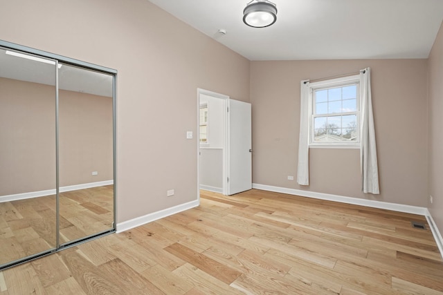 unfurnished bedroom featuring light wood finished floors, baseboards, vaulted ceiling, and a closet