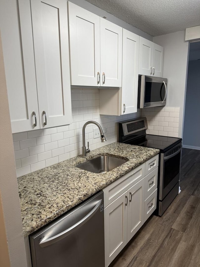 kitchen featuring appliances with stainless steel finishes, white cabinetry, sink, dark hardwood / wood-style flooring, and light stone countertops