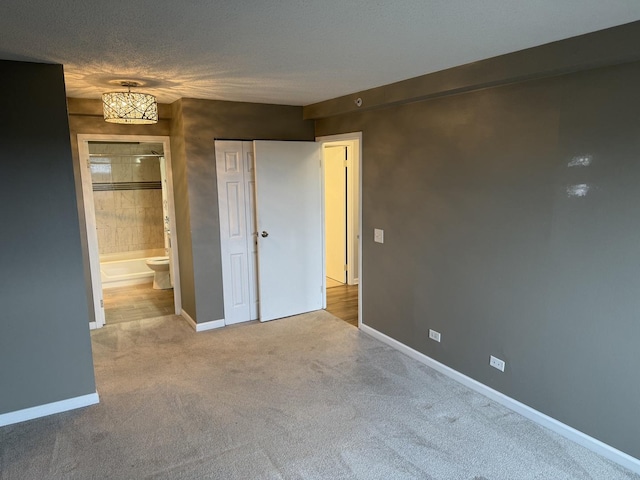 unfurnished bedroom with ensuite bathroom, light carpet, a textured ceiling, and a closet