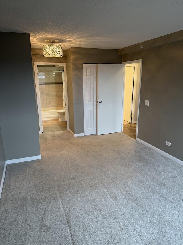 unfurnished bedroom with ensuite bath, a closet, carpet, and a textured ceiling