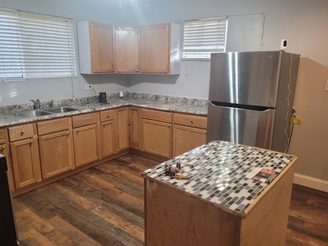 kitchen with dark hardwood / wood-style floors, light stone countertops, sink, and stainless steel refrigerator