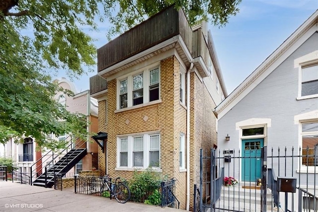 view of front of house with stairs, brick siding, and fence