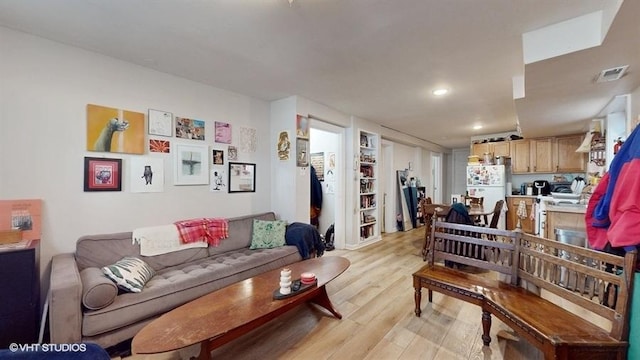 living area featuring light wood-type flooring, built in shelves, and visible vents