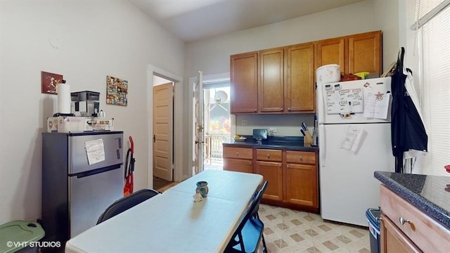 kitchen featuring dark countertops, freestanding refrigerator, and brown cabinets