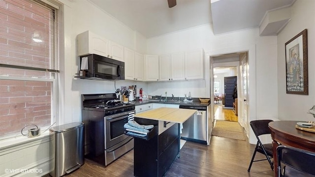 kitchen with white cabinets, dark countertops, dark wood-style flooring, a center island, and stainless steel appliances