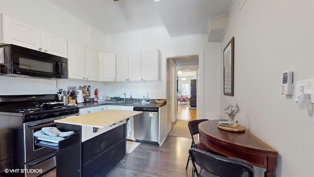 kitchen featuring dark wood-style flooring, a kitchen island, white cabinetry, appliances with stainless steel finishes, and dark countertops