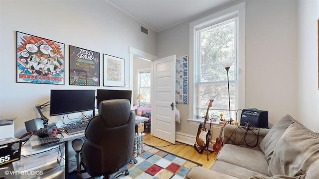 home office with light wood-type flooring, visible vents, and ornamental molding