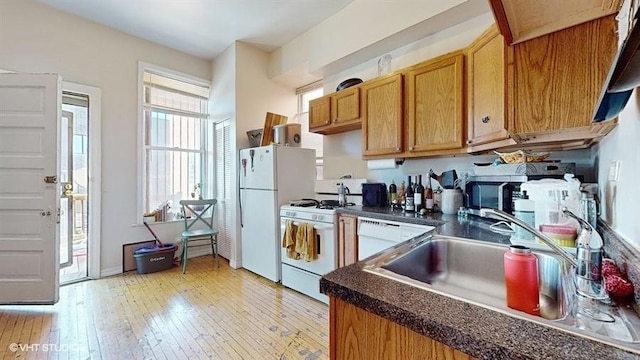 kitchen with brown cabinets, dark countertops, light wood-style flooring, a sink, and white appliances