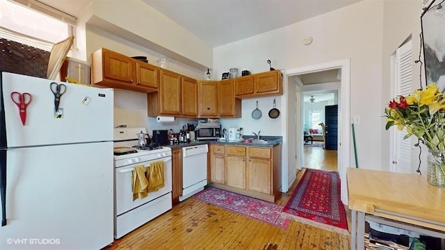 kitchen featuring white appliances, dark countertops, light wood-style flooring, brown cabinets, and a sink