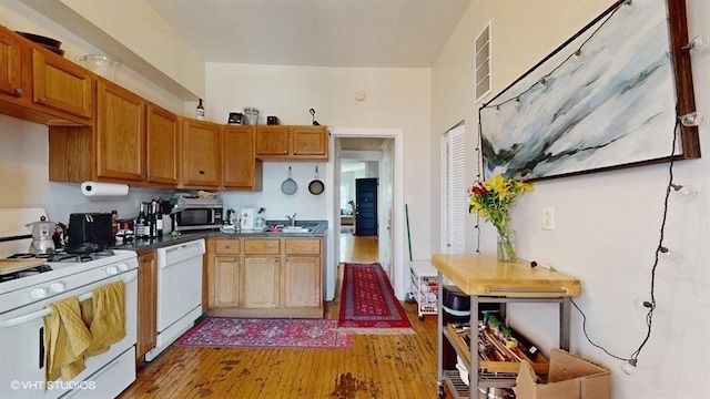 kitchen featuring white appliances, visible vents, dark countertops, wood finished floors, and a sink