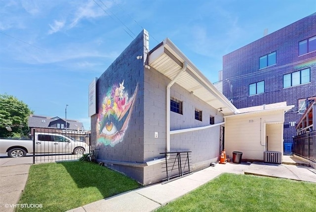 view of property exterior with central AC unit, fence, concrete block siding, and a lawn