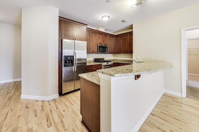 kitchen featuring light stone counters, light hardwood / wood-style flooring, stainless steel appliances, and kitchen peninsula