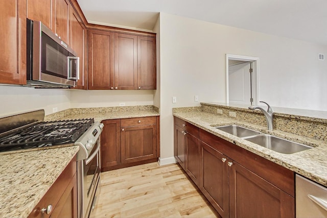 kitchen featuring light stone counters, stainless steel appliances, sink, and light hardwood / wood-style flooring