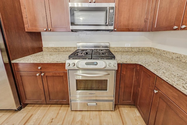 kitchen with stainless steel appliances, light stone countertops, and light wood-type flooring