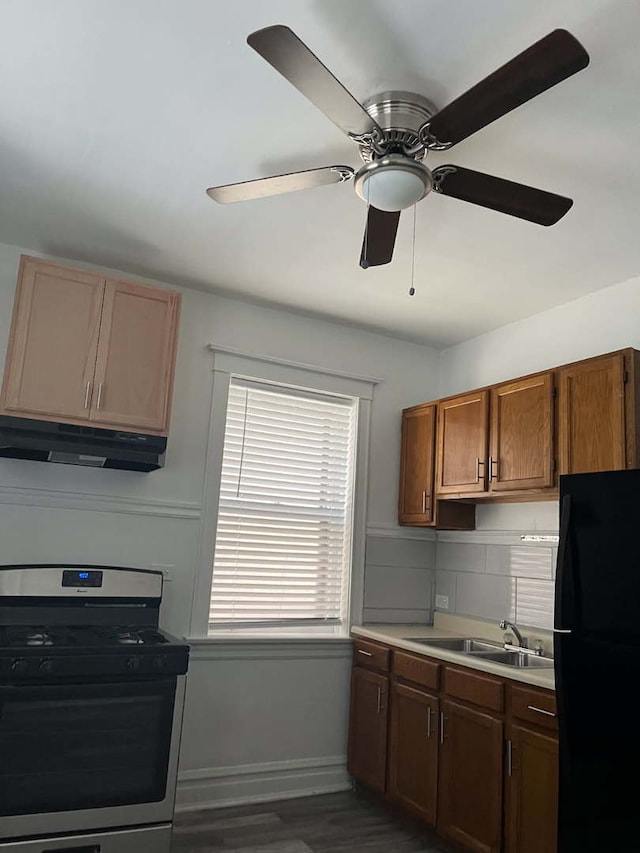 kitchen featuring black refrigerator, sink, ceiling fan, dark wood-type flooring, and stainless steel gas range