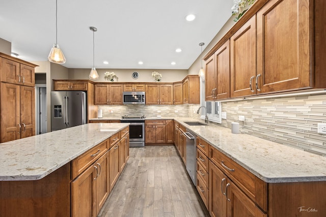 kitchen with sink, decorative light fixtures, appliances with stainless steel finishes, a kitchen island, and light stone countertops