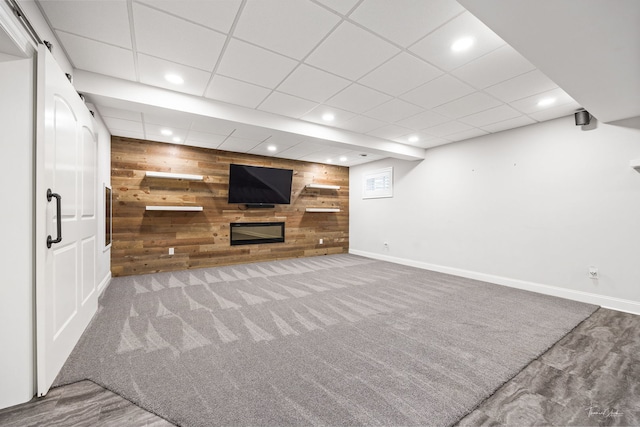 unfurnished living room featuring carpet, a drop ceiling, and wooden walls