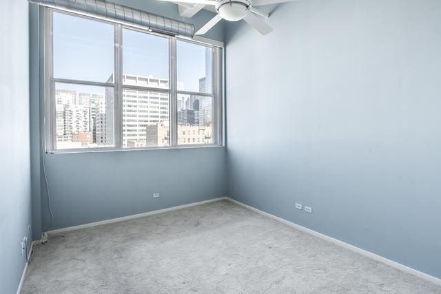 unfurnished room featuring a ceiling fan, carpet, a healthy amount of sunlight, and a view of city