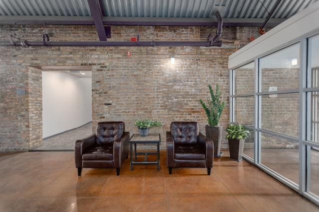 living area with brick wall, beam ceiling, and concrete flooring